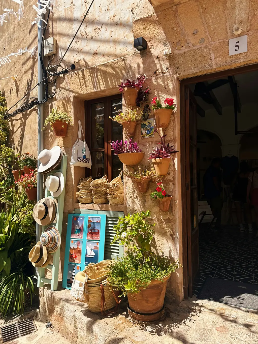 Ladeneingang mit Strohhüten und Pflanzen in einer Gasse aus Naturstein