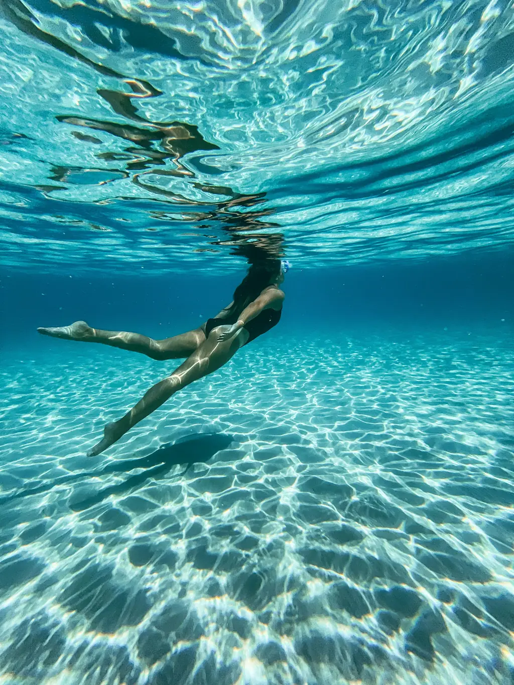 Schwimmerin unter Wasser über hellem Sandgrund